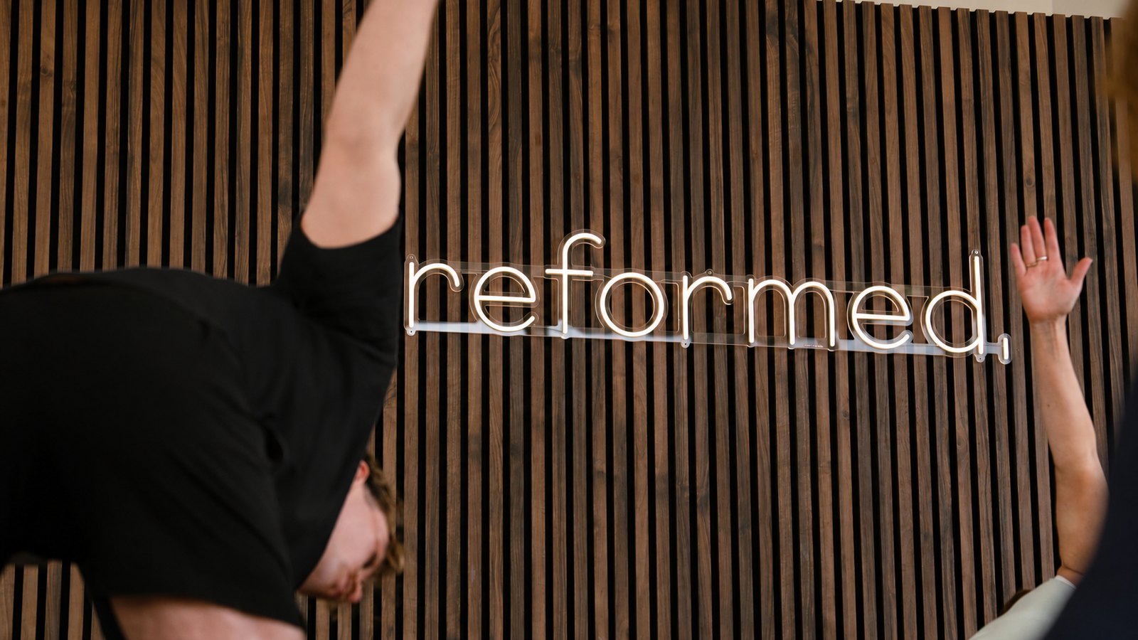 Reformed. studio brand wall — neon sign on dark oak slats with figures mid-pose